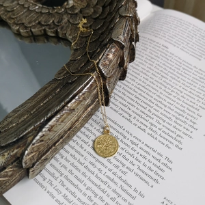 Detail of vintage gold coin pendant necklace resting on art book with decorative frame
