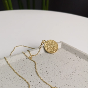 Detailed close-up of a vintage golden six pence coin pendant on a delicate link chain necklace