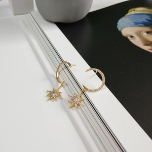 Close-up of golden C-shaped star moon earrings with white zircons on a creative background