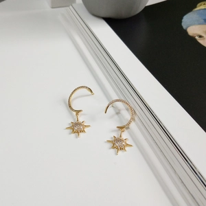 Detailed view of gold sterling silver star and moon earrings on a white book edge