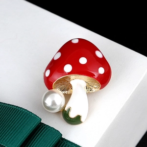 Macro detail of red mushroom brooch with white dots and elegant pearl accent on side