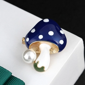 Detail of mushroom brooch with blue enamel white dots and a lustrous pearl on a white stand