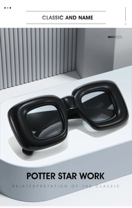 Detail of Y2K wrap sunglasses with chunky black frames and dark lenses on a geometric stand
