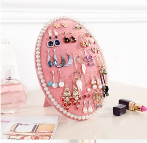 Pink velvet oval earring holder with pearl edge decor in a luxury dressing table setup