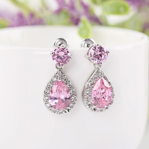 Pink teardrop zircon earrings with silver accents hanging on a white ceramic cup