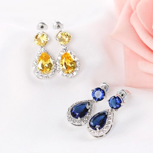 Detailed view of pear-cut yellow and blue drop earrings on soft white silk fabric