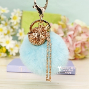 Détail du porte-clés pompon bleu clair avec un pendentif cloche en métal doré ajouré