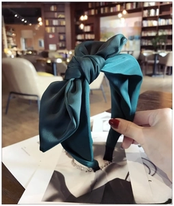 Macro detail of the dark green satin fabric texture and large bow knot on the headband