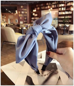 Detail of gray-blue satin fabric headband with a wide twisted bow in a cozy indoor setting