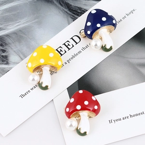 Detail of red, yellow and blue mushroom brooches with pearl accents on a card