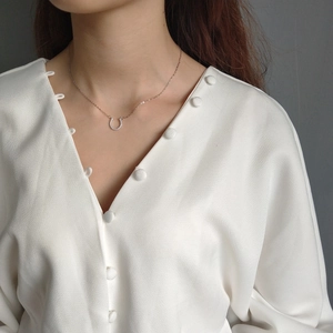 Detail of a gold horseshoe necklace with white stones worn on a woman's collarbone