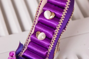 Close-up of gold heart stud earrings displayed on a purple high heel jewelry holder