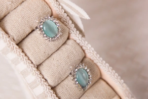 Detailed view of mint green oval stud earrings with crystal halo on jewelry stand