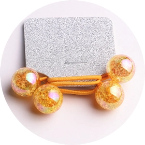 Detail of yellow elastic hair tie with four golden foil amber-like beads on glitter card