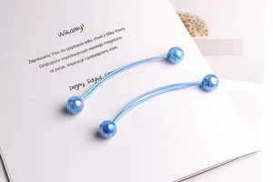 Detail of two elastic blue hair ties with shiny blue spheres on a white paper background