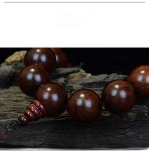 Close-up of polished rosewood prayer beads with a glassy finish on a natural wood base