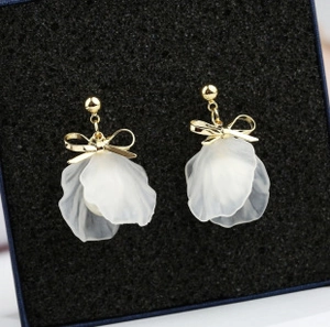 Detailed shot of elegant gold bow earrings with white translucent flower petal charms