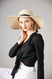 Elegant wide brim straw sun hat with black ribbon detail shown on a female model
