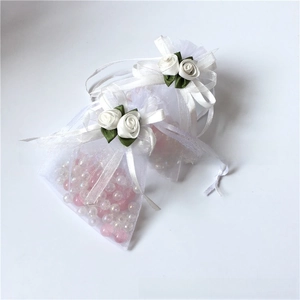 Close-up of white organza drawstring pouch featuring a handmade ribbon rose and pearls