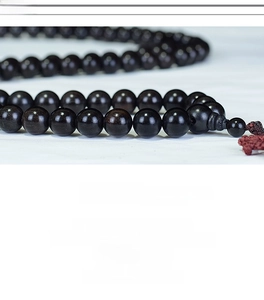 Macro shot of 108 polished black ebony beads showing natural wood grain and oily texture