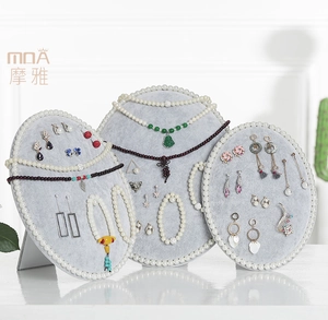 Close-up of oval gray velvet jewelry display stand with elegant pearl trim decoration