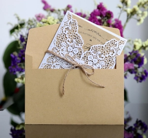 Detail of laser-cut wedding invitation with kraft envelope, twine bow and floral accents