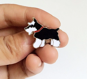 Détail d'une broche chien en émail noir et blanc avec collier rouge et bordure dorée