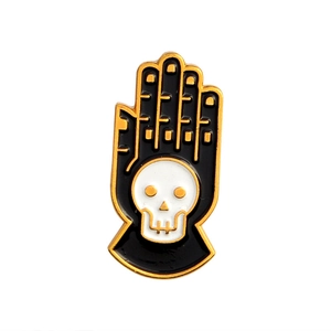 Enamel skull hand badge with black palm and gold trim on white background