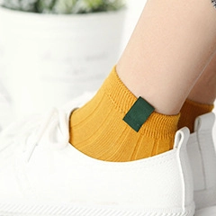 Close-up of yellow ribbed knit cotton socks with a green woven label and sneakers