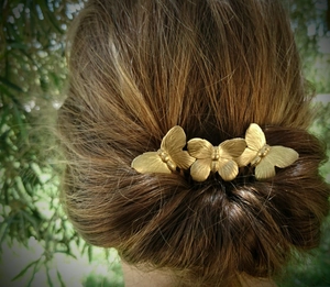 Detail of three vintage matte gold butterfly hair clips worn on brunette hair
