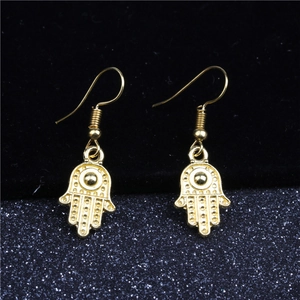 Detailed view of golden Hamsa Hand hook earrings on a dark textured background