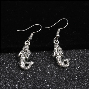Dettaglio di orecchini a sirena in argento vintage con texture a scaglie su sfondo nero