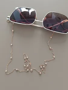 Detail of gold metal glasses chain with small beads on dark wood surface background