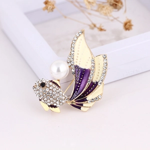 Macro view of a gold-tone fish brooch with a gradient tail and a white faux pearl inlay