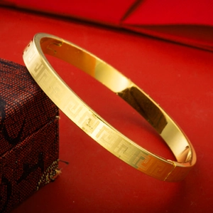 Bracelet doré avec motif de méandres grecs présenté sur une boîte à bijoux rouge de luxe