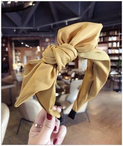 Detail of a mustard yellow fabric headband featuring a large bow and soft satin texture