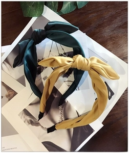 Close-up of wide bow headbands in dark green and mustard yellow satin fabric