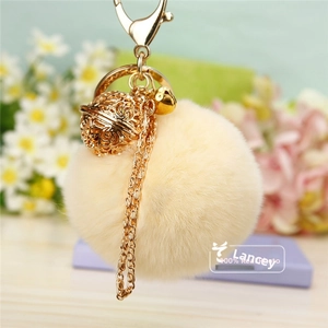 Détail macro du pompon en fausse fourrure beige avec breloque fleurie dorée et clochette