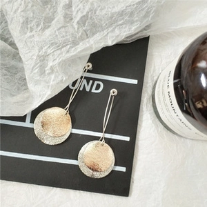 Detail view of long textured earrings with silver and gold metallic circular disks