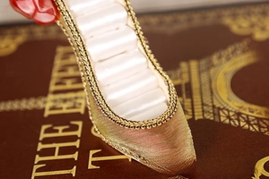 Detailed close-up of high heel ring display stand with gold textured fabric and satin slots