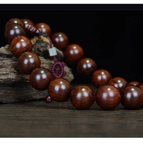 Macro detail of polished rosewood prayer beads showing deep red wood grain and glossy finish