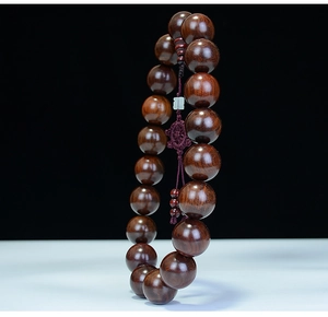 Macro detail of polished rosewood prayer beads with a jade pendant and a red knot