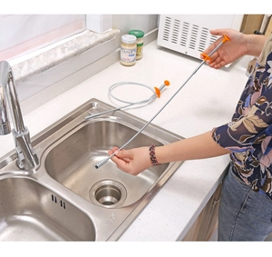 Flexible metal sewer claw tool with orange handle being used in a kitchen sink