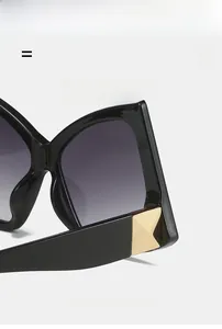 Close-up of black oversized square sunglasses showing golden metal accents on the temple
