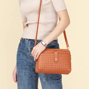 Handwoven orange-brown leather crossbody bag with metal buckle and shoulder strap