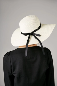 Close-up of a white wide-brimmed straw hat with a black ribbon bow for sun protection