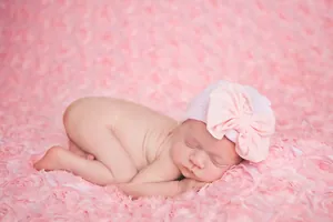 Macro shot of newborn knitted hat featuring a large pink bow on lavender fabric