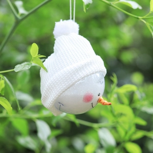 Close-up of a snowman ornament with a white knit hat hanging on a green branch