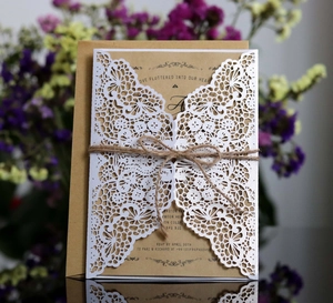Detail of laser-cut white lace wedding invitation with kraft paper and hemp rope bow