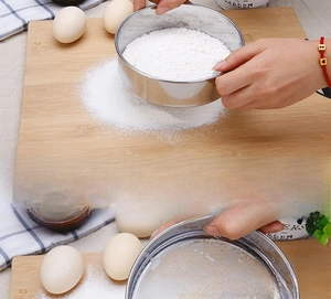 Close-up of hand using a 60 mesh stainless steel flour sifter for fine baking